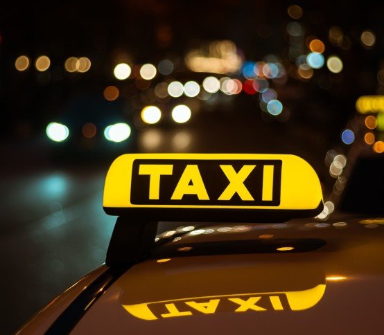 A yellow and black sign of Taxi placed on top of a car at night